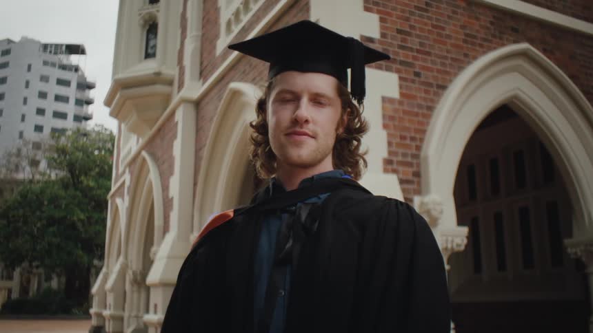A graduate wearing a cap and an academic robe poses for the camera