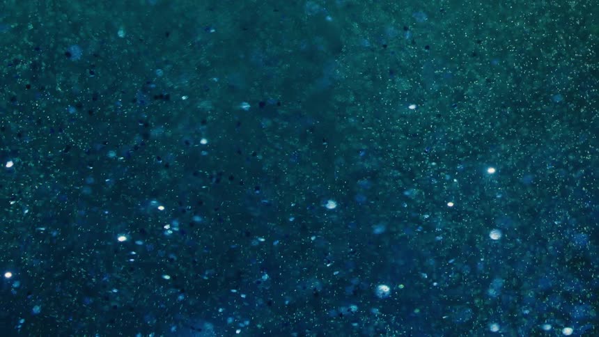 Dark blue liquid is sprinkled with small blue sparkly dots