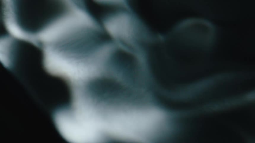 White textured mass creates bubbles while flowing through a liquid in the darkness
