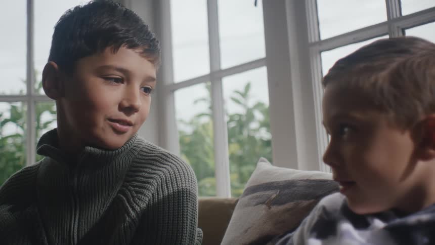 Two boys sit and talk near a window
