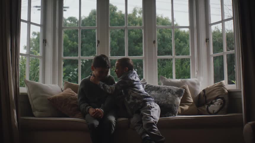 A young child whispers in his friends ear in the living room