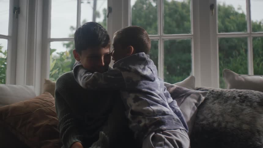 Boy running towards his friend who is sitting on the couch and whispering in his ear