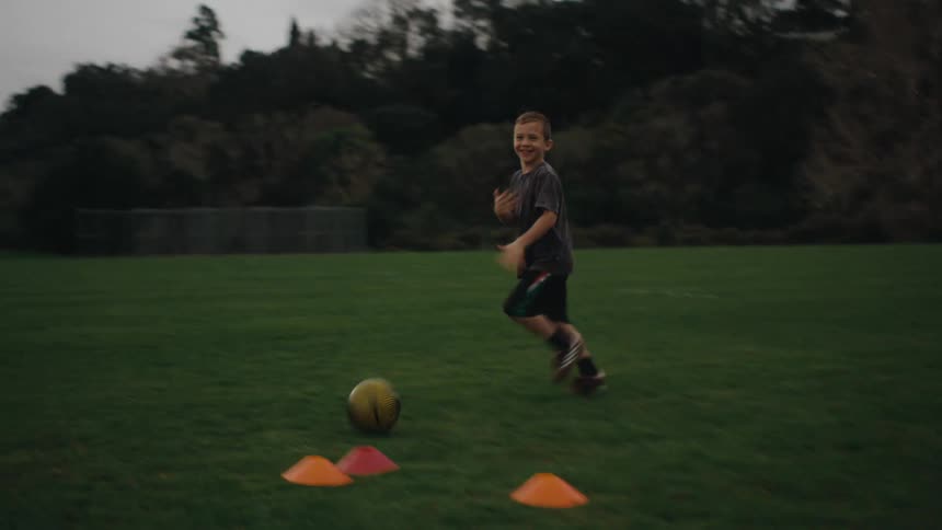 A boy in a black uniform runs across a green field during soccer practice