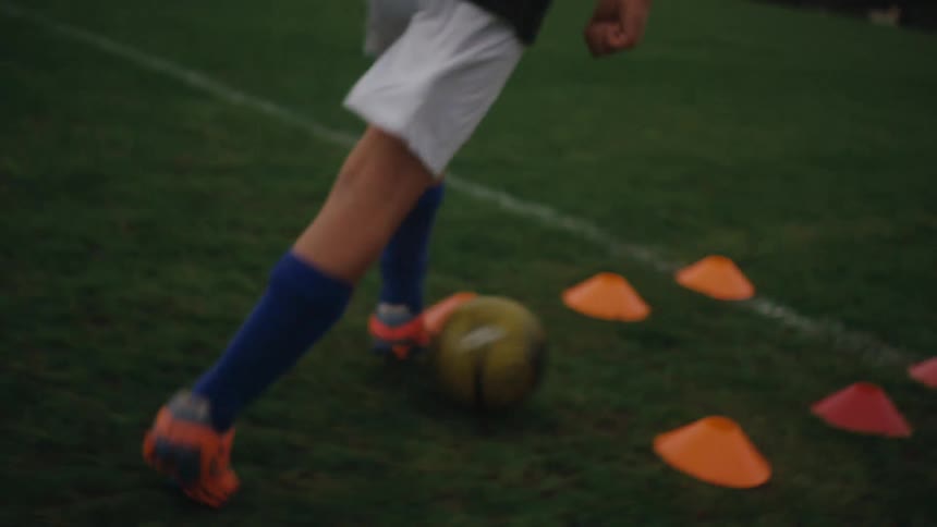 Legs of a boy dribbling around cones on a grass field
