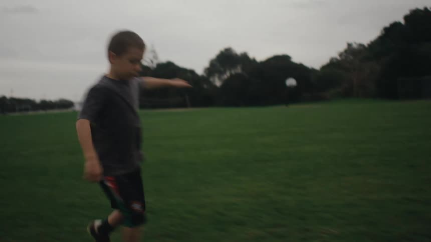 Child dribbling a football on a football pitch on a cloudy day