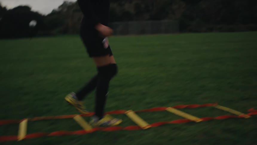 Girl jumping on top of a ladder on the grass in warm up