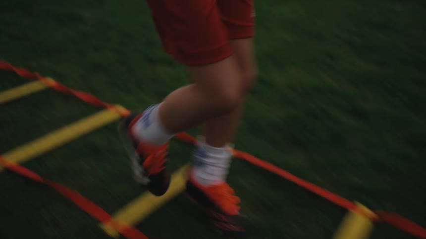 A boy runs over a ladder lying on the ground while two of his friends watch