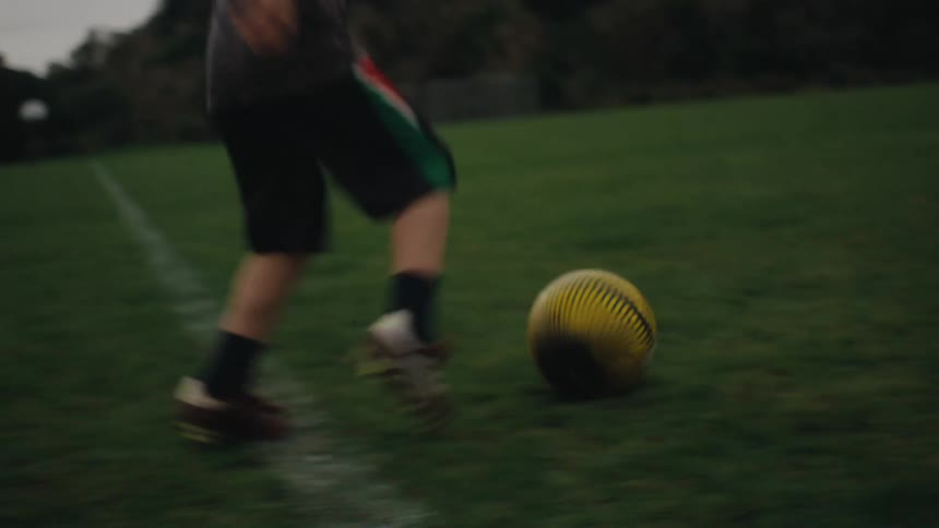 Young boy is running with a soccer ball and kicks it towards another boy standing at the goal