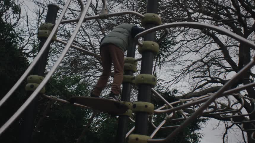 Child in openair playground with trees in the background playing jumping