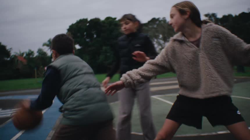 Tall girl plays basketball on an outdoor court at the park with other children