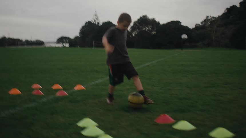 Children practicing soccer on a green field running between cones placed for drills