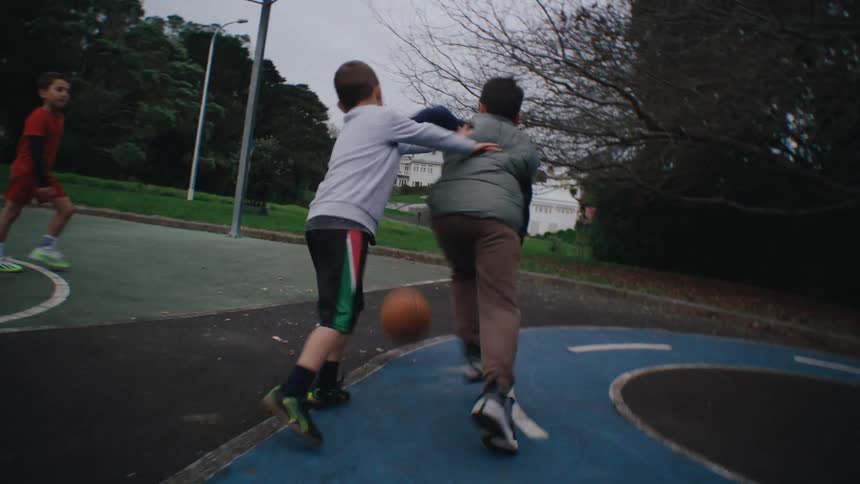 Kids playing basketball in the park on a cloudy day
