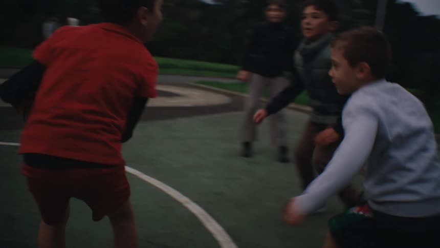 Kids play basketball on an outdoor court near a leafless tree in the park