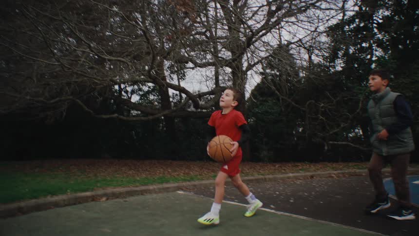 Two boys playing basketball with one of them throwing the ball towards the basket
