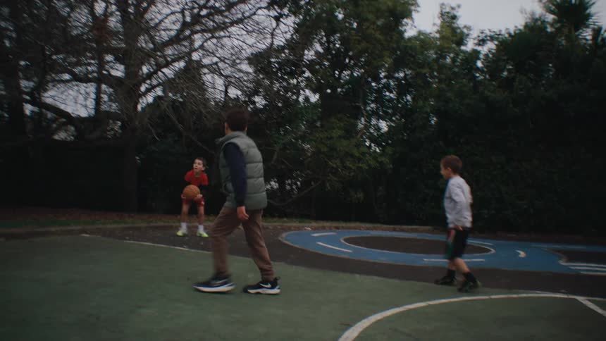 Children playing basketball and a court with trees in the background