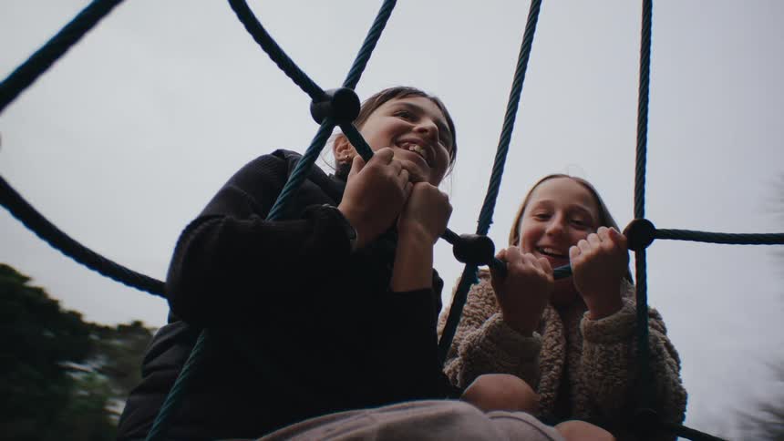 Two girls holding on to a rope on a spinning toy in a playground