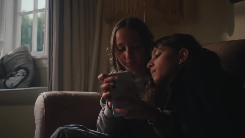 Two girls sitting interacting with smartphone