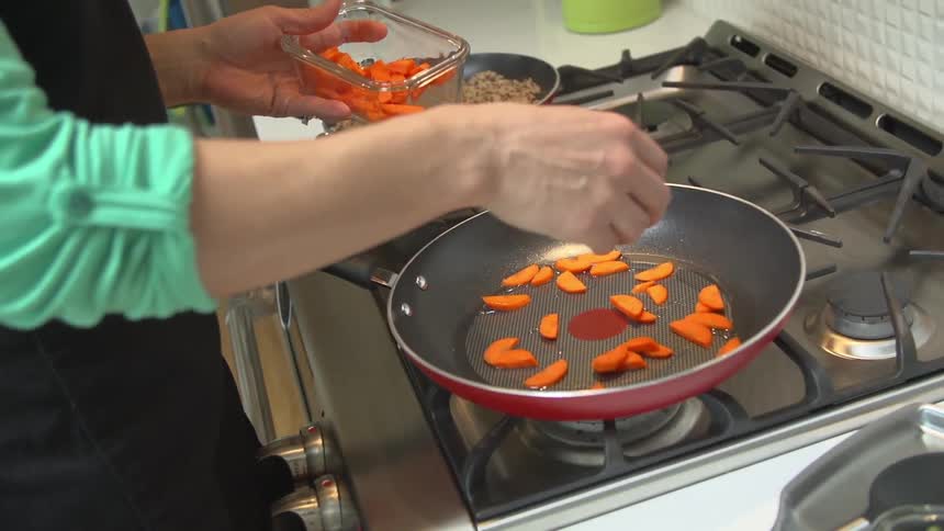 A woman cooks carrots in a skillet