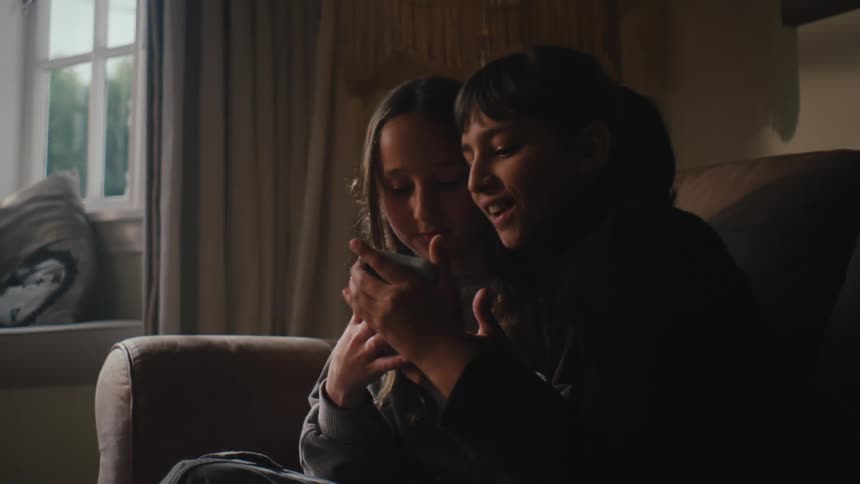 Two girls sitting on a couch looking at a smartphone