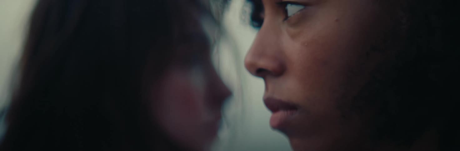 The intense expression of one person in focus while another figure appears blurred in the background adding a sense of mystery and depth to the scene