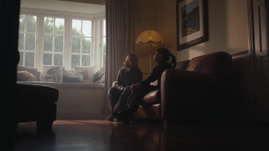 Friends embrace before sitting on a leather couch in a living room