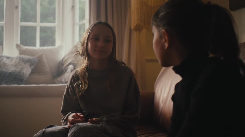 Two people sit in conversation near a window with soft natural lighting