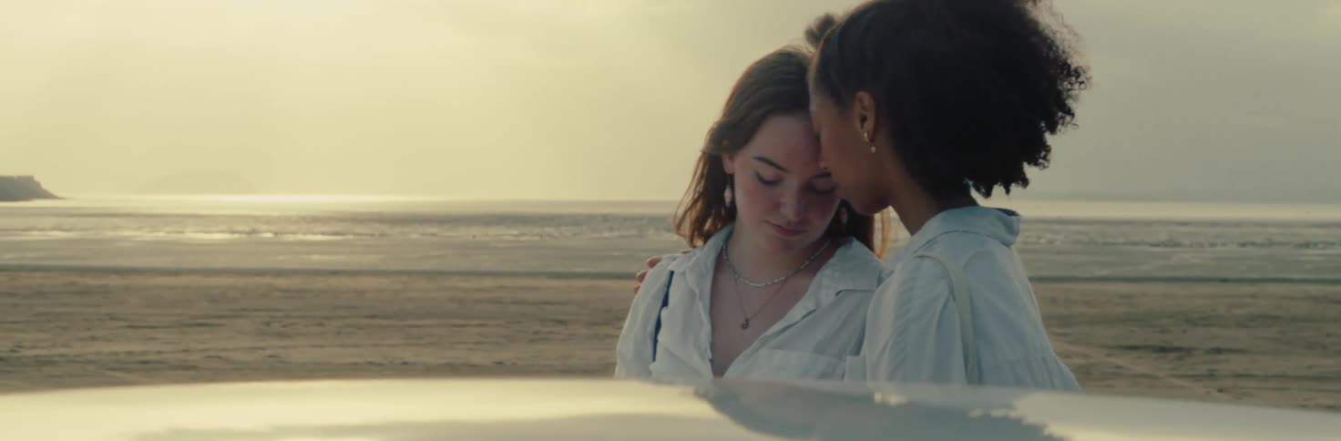 A couple shares a tender moment by a car parked on a beach at sunset