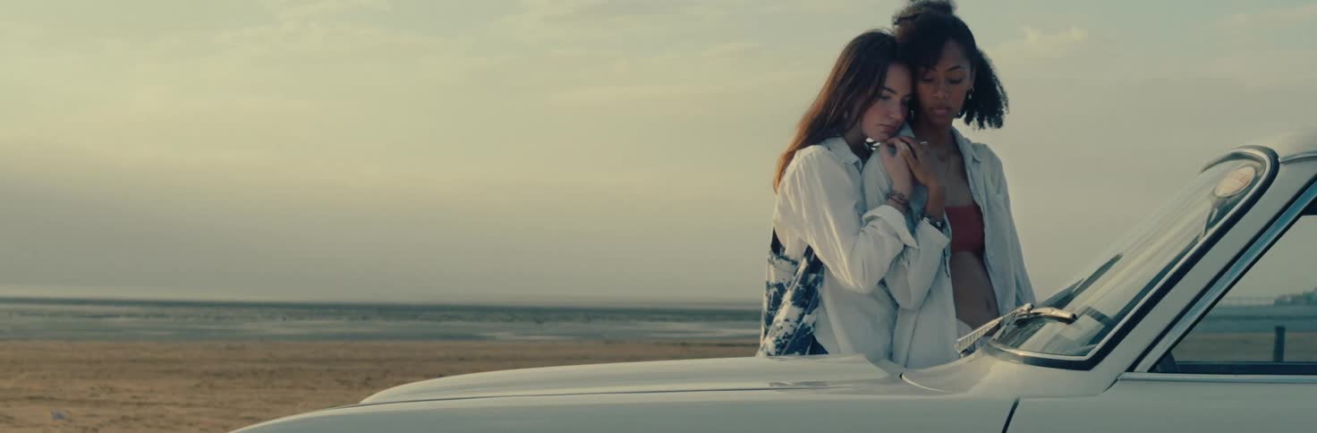 Two women hugging next to a car on the beach