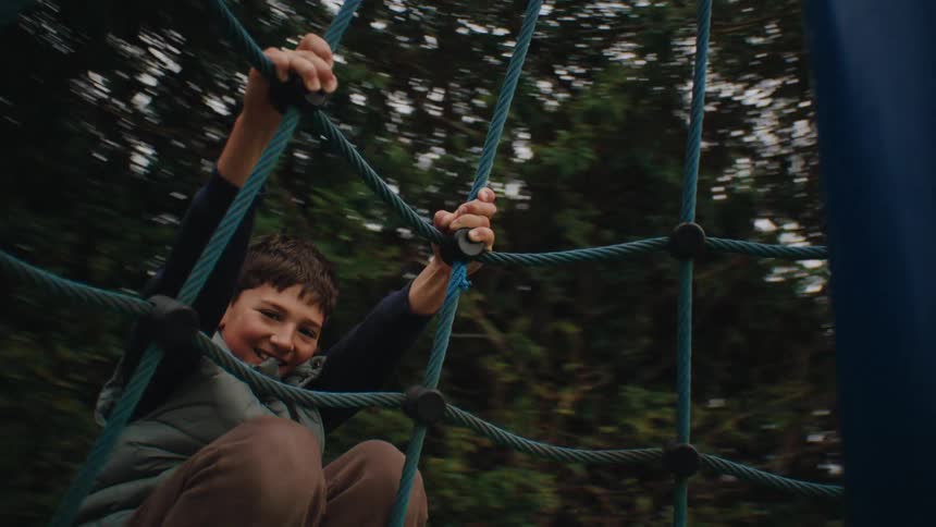 Boy playing holding on to the ropes of a spinning toy in a park
