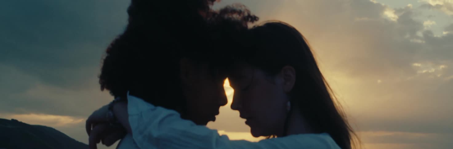 Couple embrace with foreheads touching with the sunset behind them