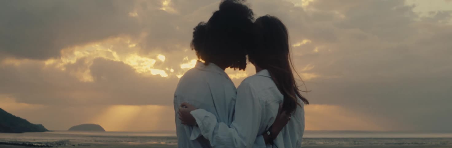 Female couple hugging watching the sunset over the ocean