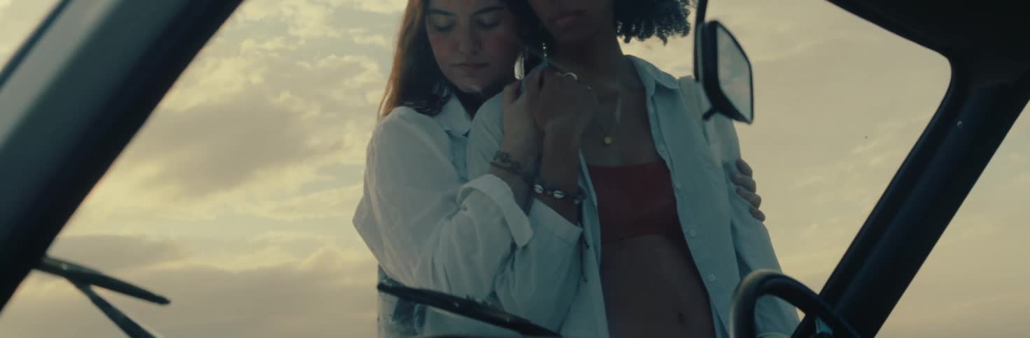 Two women stand holding hands as seen through car window