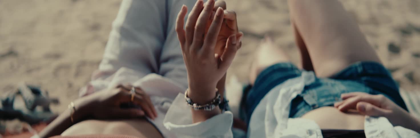 Two women holding hands while sitting on the sand at the beach