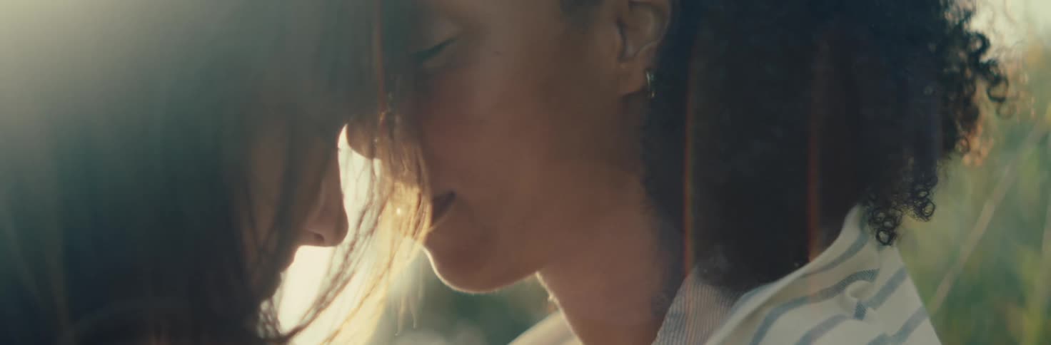 Two females are standing nose to nose with their eyes closed backlit by sunlight