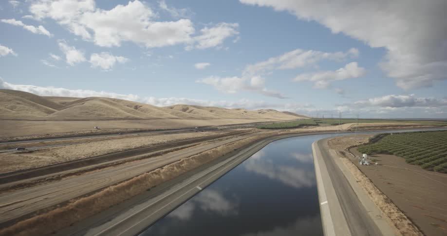 Aerial panorama of a water channel surrounded by mountains and an agricultural field