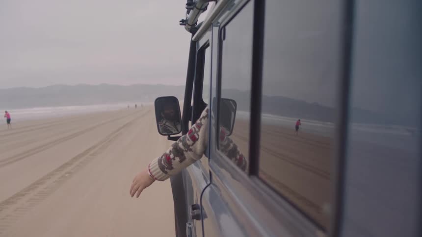 A man drives on a beach road with his arm out the window