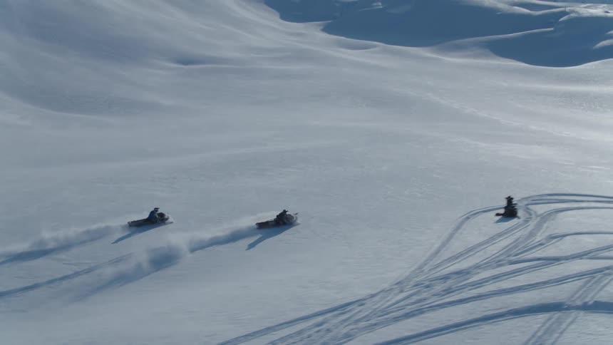 Aerial of people riding snowmobiles in a mountain valley on a winter day