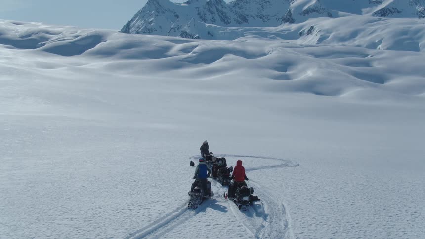A group of people ride snowmobiles across a vast snowy landscape