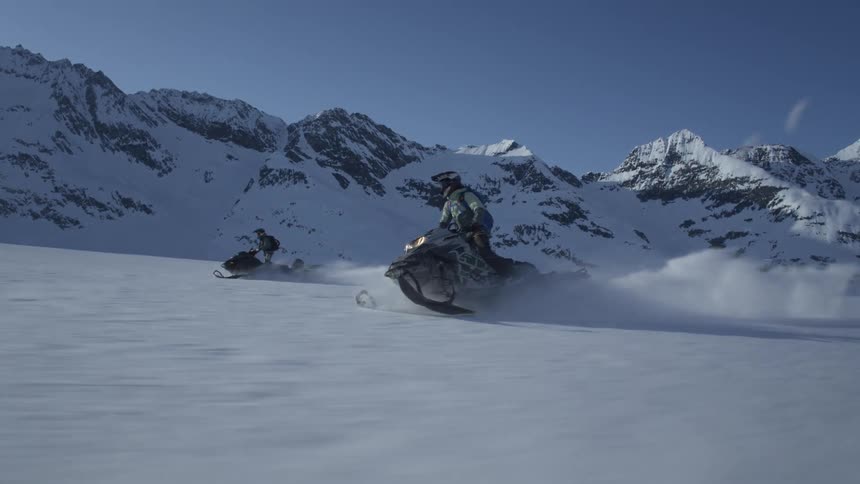 Snowmobile riders navigate the vast expanse of snowcovered terrain with mountain peaks forming a dramatic backdrop under a clear blue sky