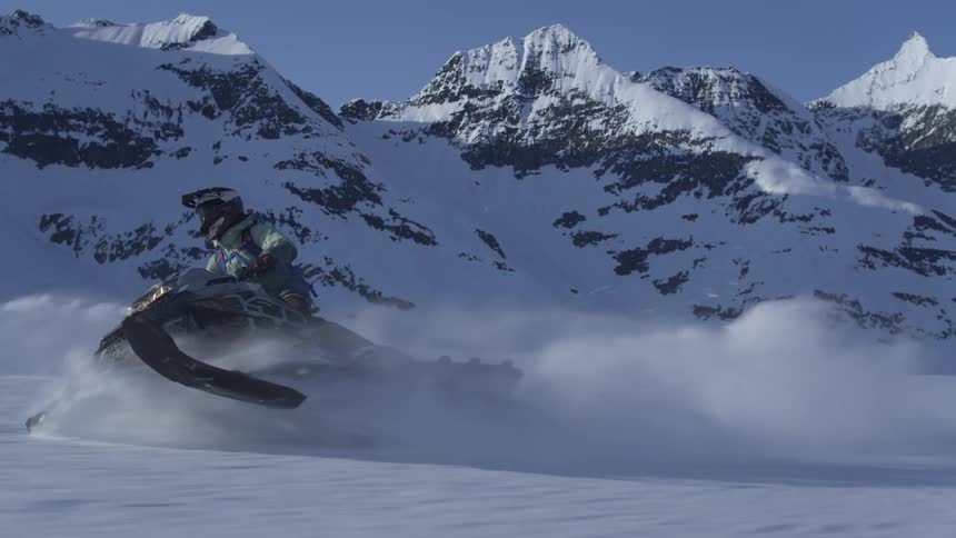 A group of people riding a snowmobile across a snowy landscape with mountains in the background