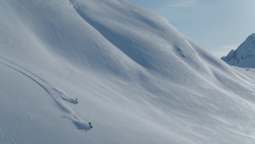 Two people on snowmobiles descending a large snowy mountain