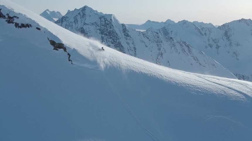 A snowmobile climbs a steep snowy slope with rugged mountains in the background