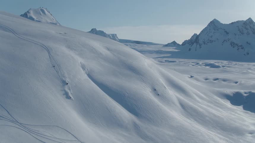 A snowmobile descends a steep snowy slope with rugged mountains in the background