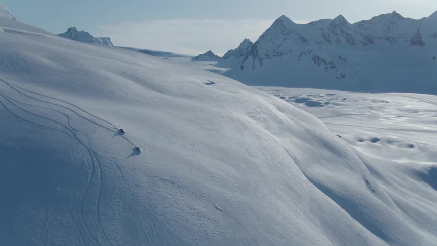 Aerial view of two people on snowmobiles riding through the arctic