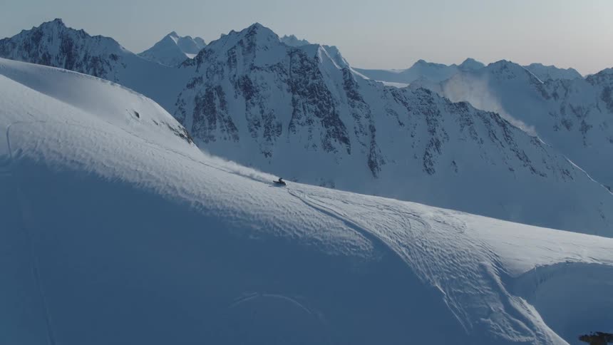 Snowy mountain landscape with rugged peaks and clear sky and a person riding a snowmobile