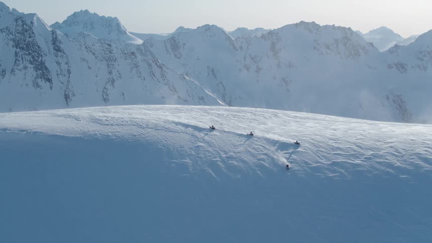 Group of people on snowmobiles descending a snowy mountain