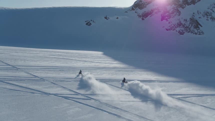 A small group of people are snowmobiling in a mountain valley on a sunny winter day