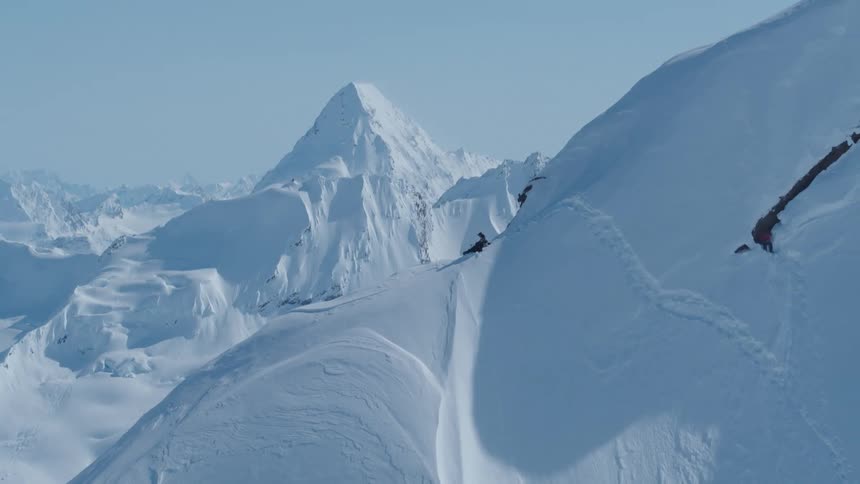 Two people with ski equipment on a snowy mountain peak