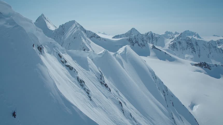 Aerial view of two people climbing towards the peak in a snowy mountain valley