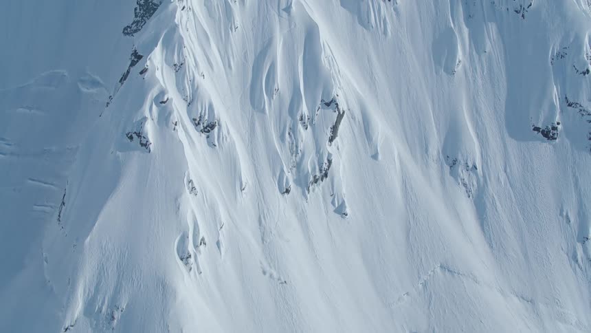 A skier descends a steep snowcovered mountain slope with visible rock outcrops